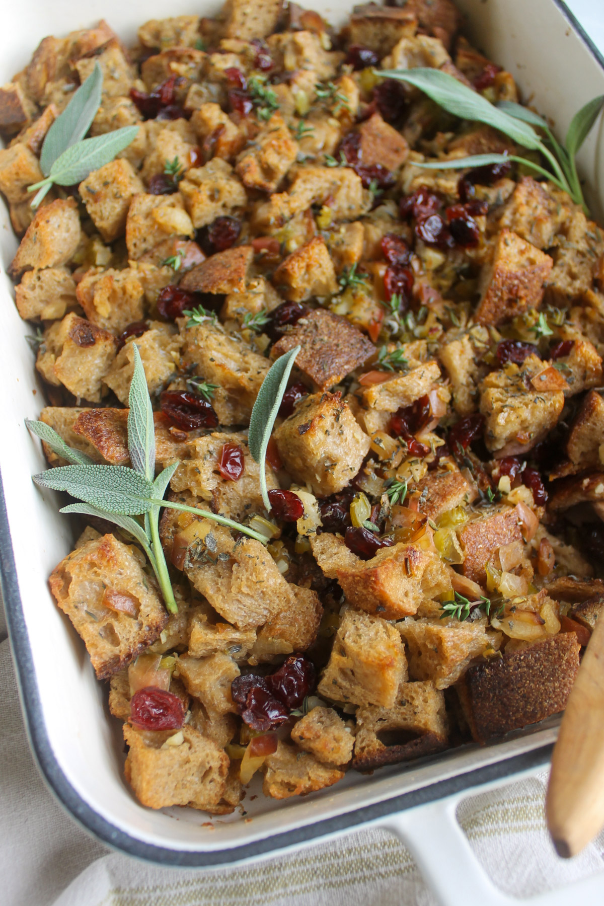 Bread stuffing in a white baking dish with red dried cranberries.