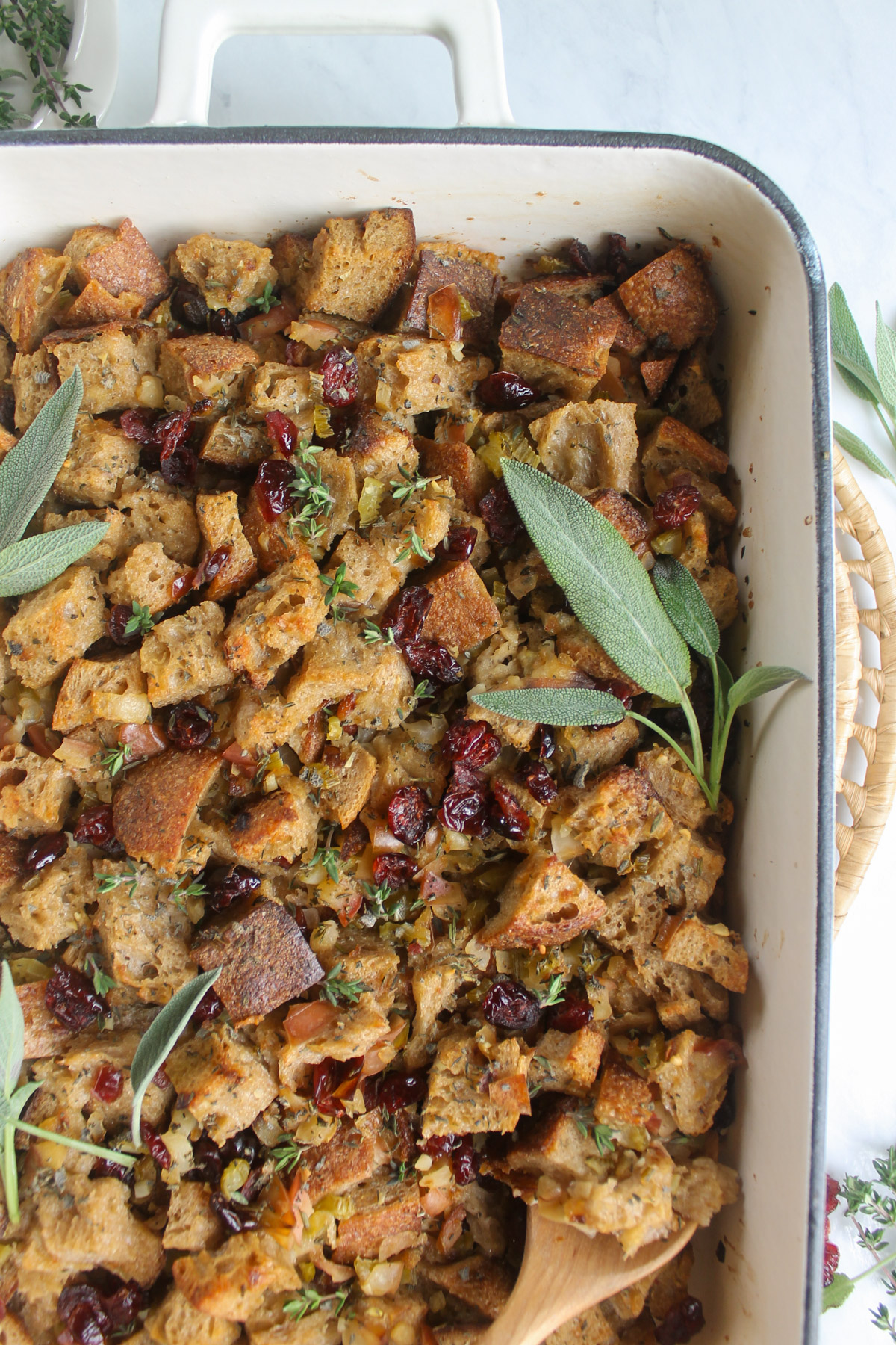 The corner of a white baking dish of stuffing topped with fresh sage.