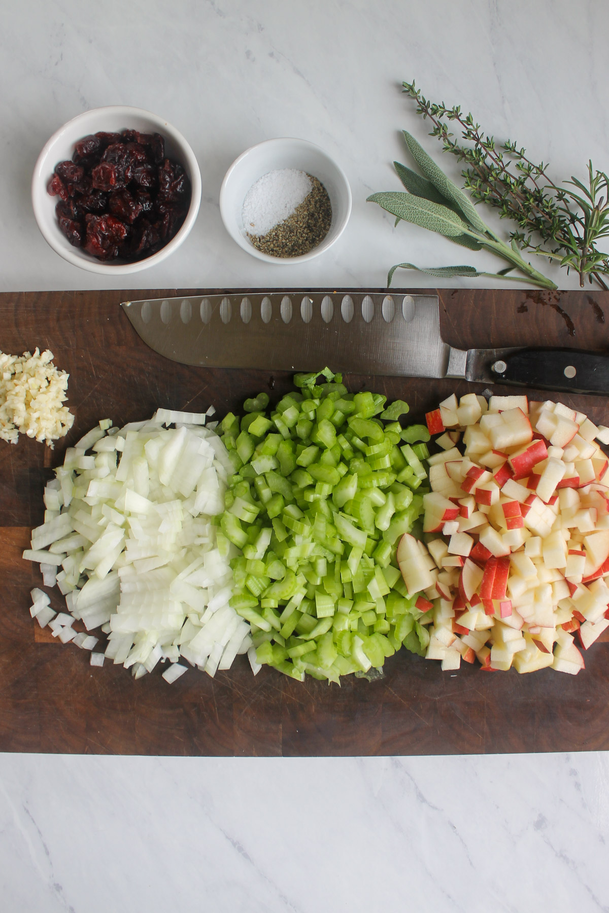 Chopped onion, celery, apple and garlic on a cutting board with a knife and other ingredients.