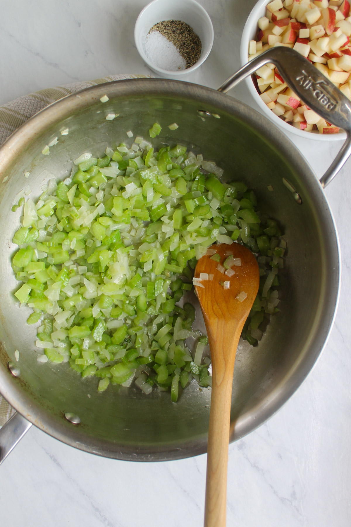 Onions and celery sautéing in a skillet with a wooden spoon.