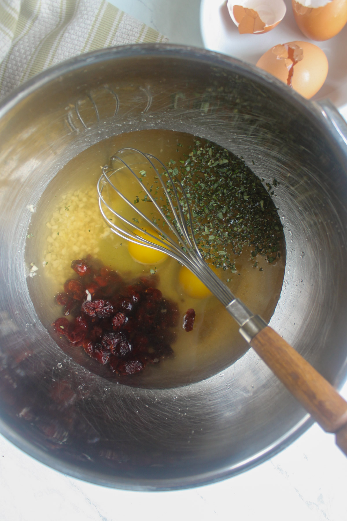A large mixing bowl with eggs, stock, dried cranberries, garlic and a whisk.