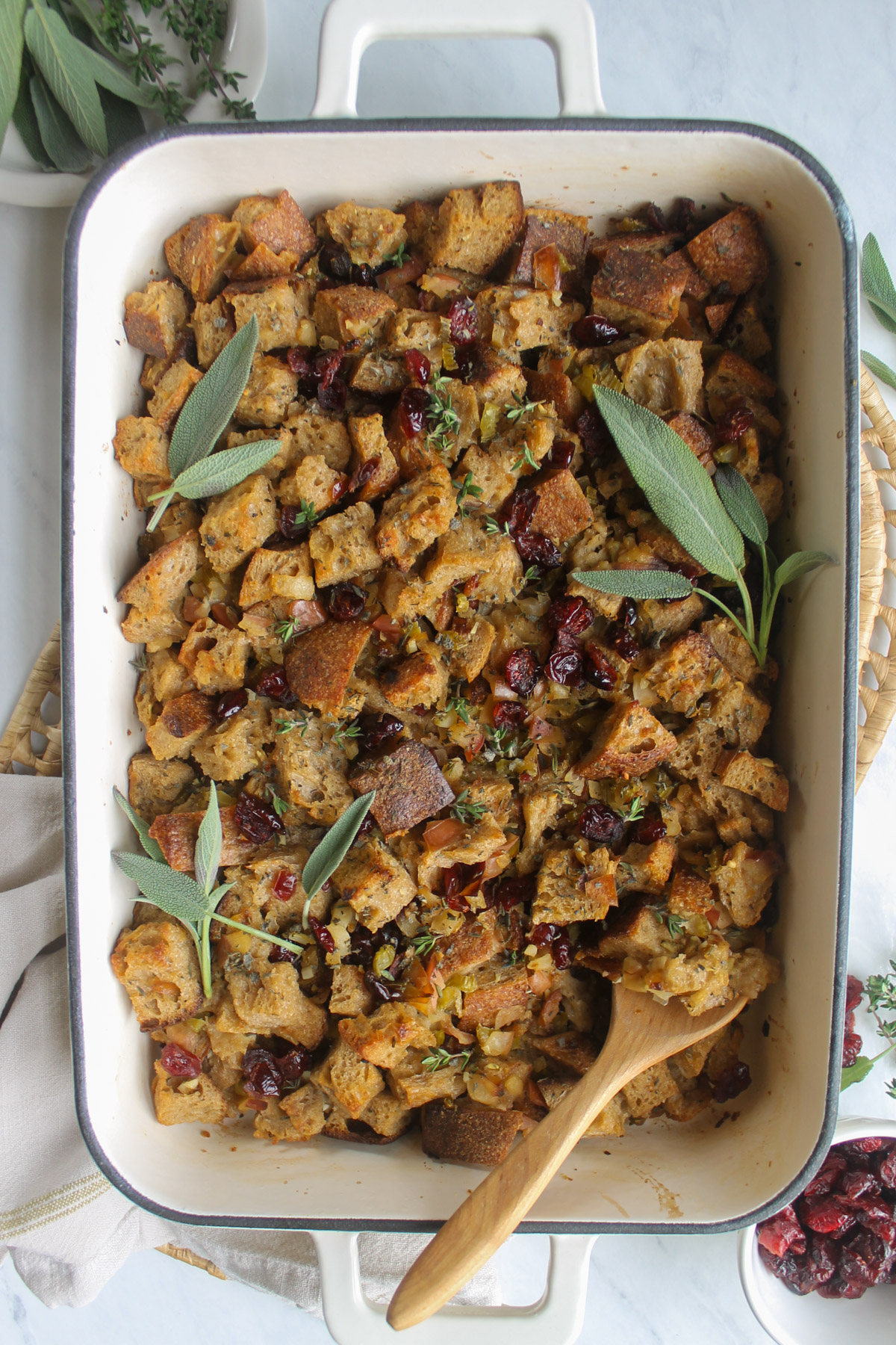 Baked Cranberry Herb Bread Stuffing topped with herbs and a wooden serving spoon.