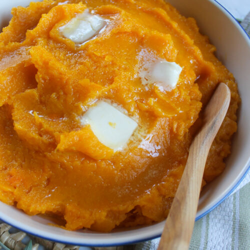 A bowl of orange mashed butternut squash with butter.