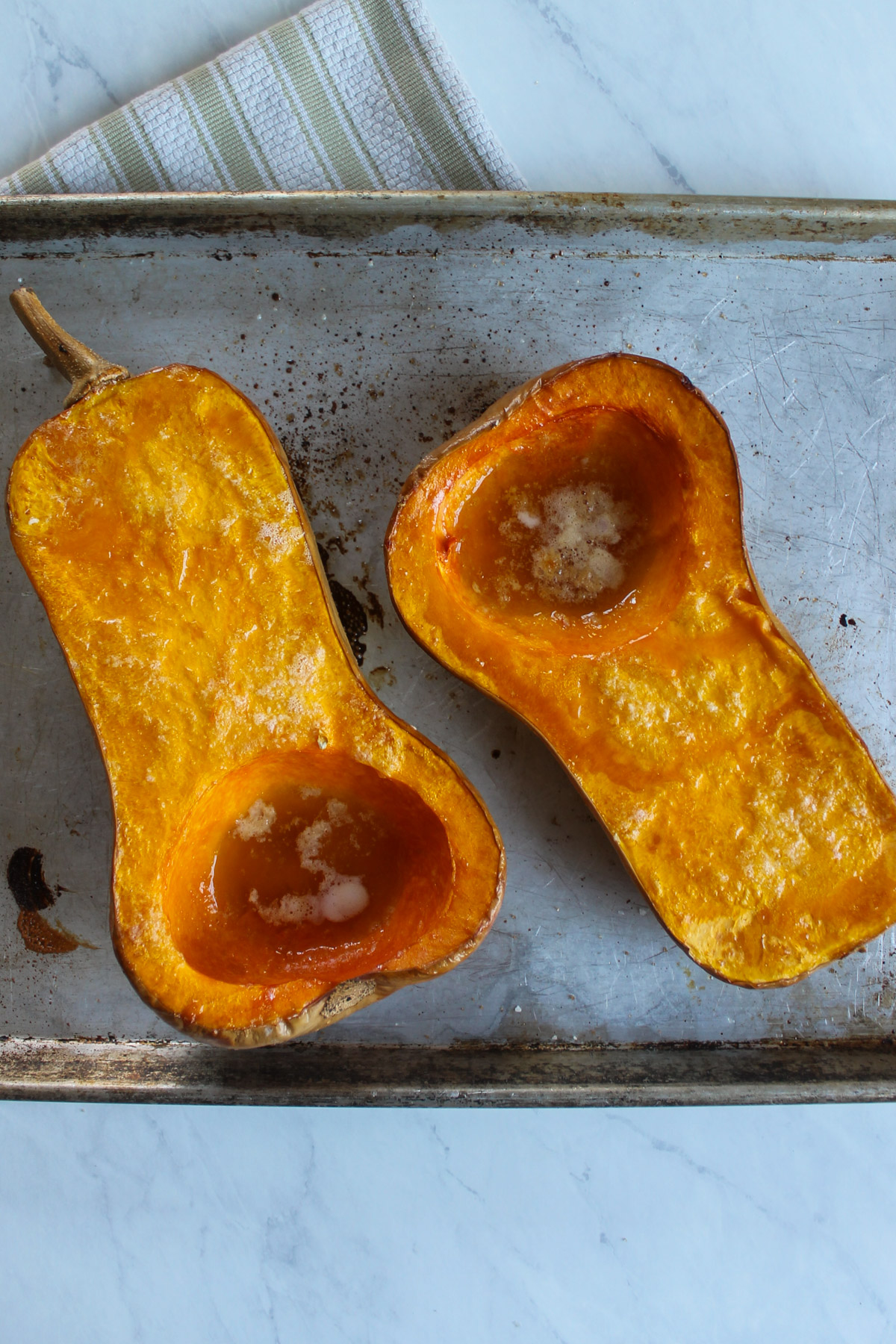 Two halves of roasted butternut squash on a sheet pan.