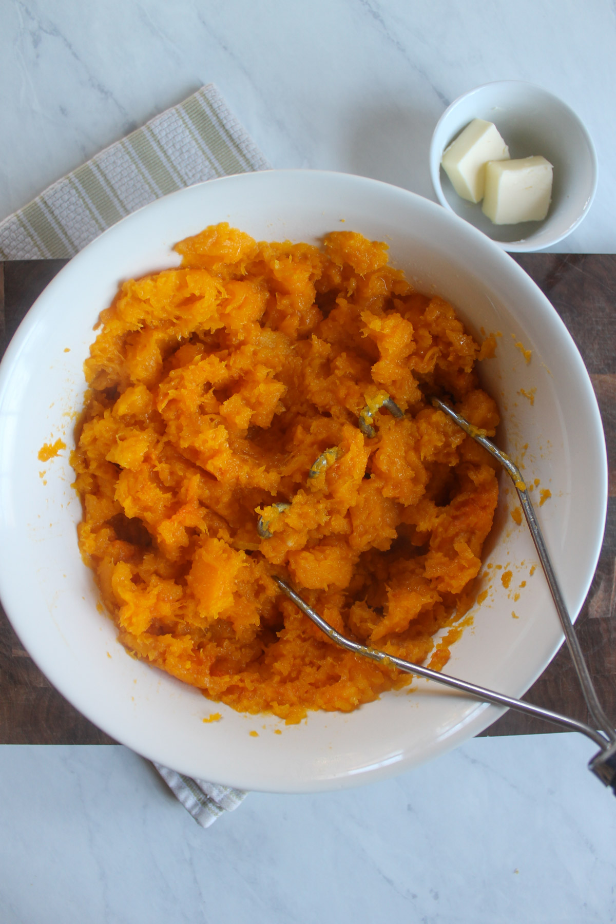 Mashing butternut squash in a bowl with a potato masher.