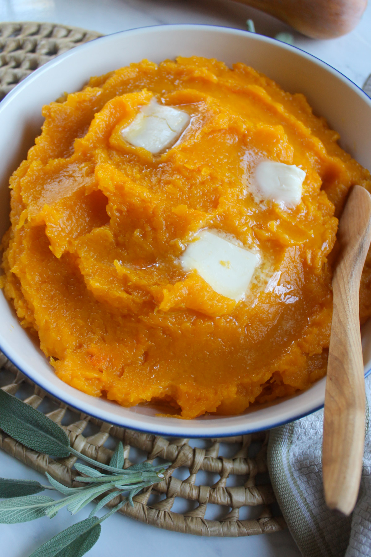 A white bowl of mashed butternut squash topped with pats of melting butter.