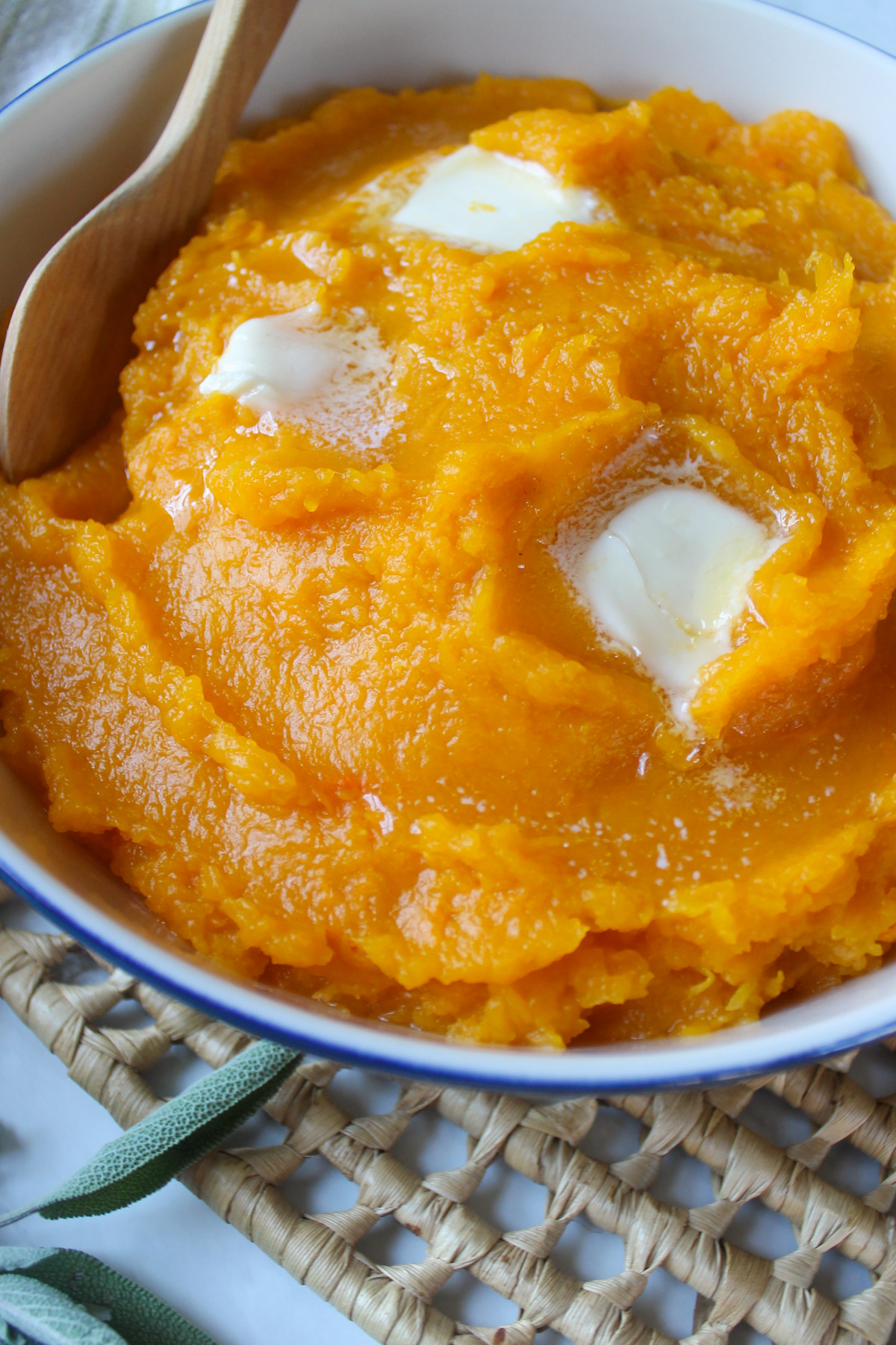 A white bowl of mashed butternut squash with butter and a wooden spoon.
