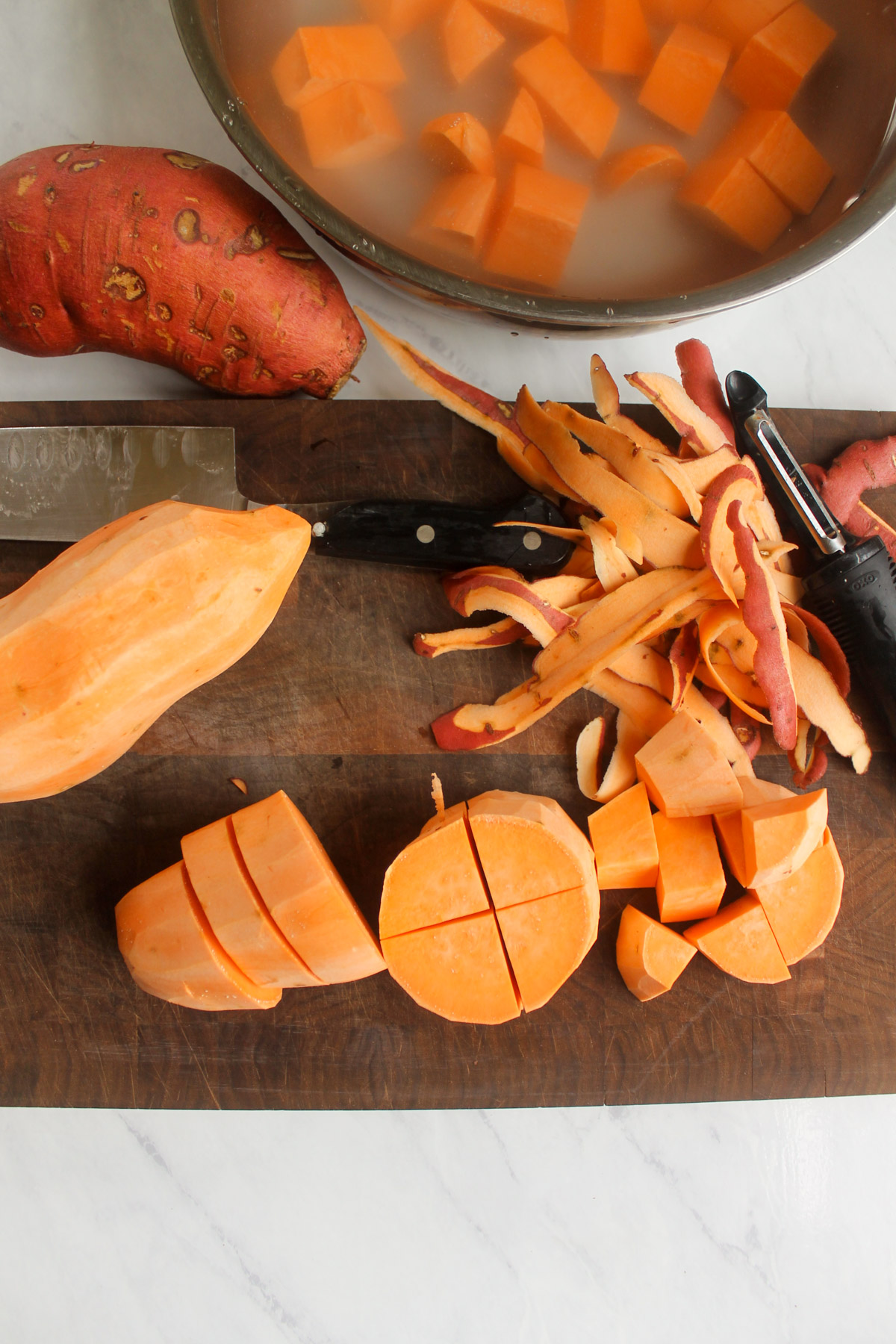 Peeling and chopping sweet potatoes on a cutting board.