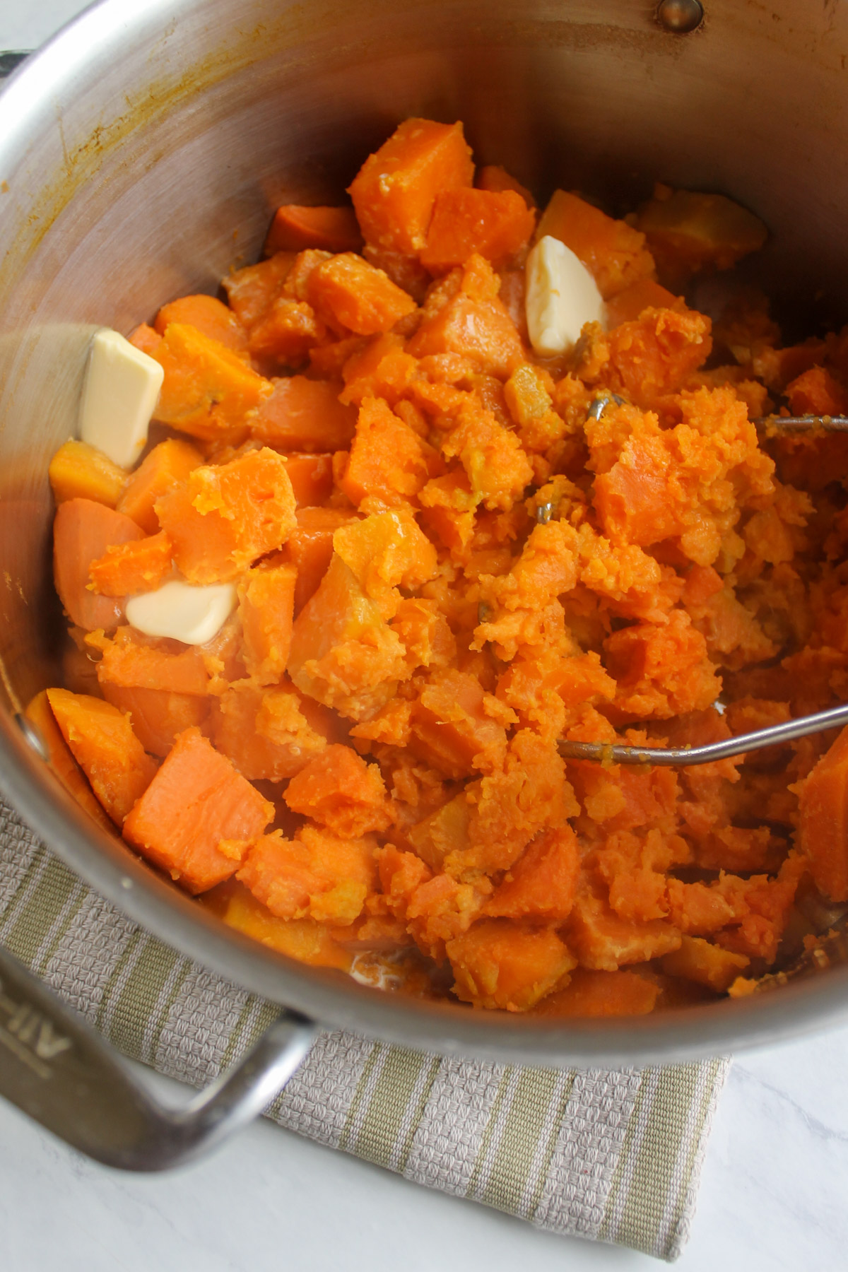 Mashing sweet potatoes with butter in a large pot with a potato masher.