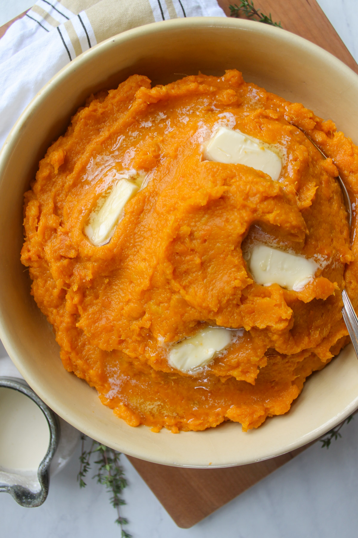 A bowl of mashed sweet potatoes with pats of melting butter.