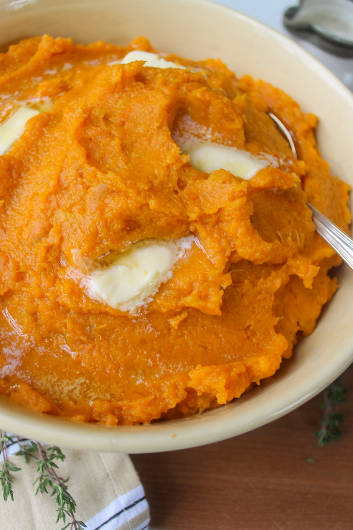 A bowl of mashed sweet potatoes on a wooden cutting board.
