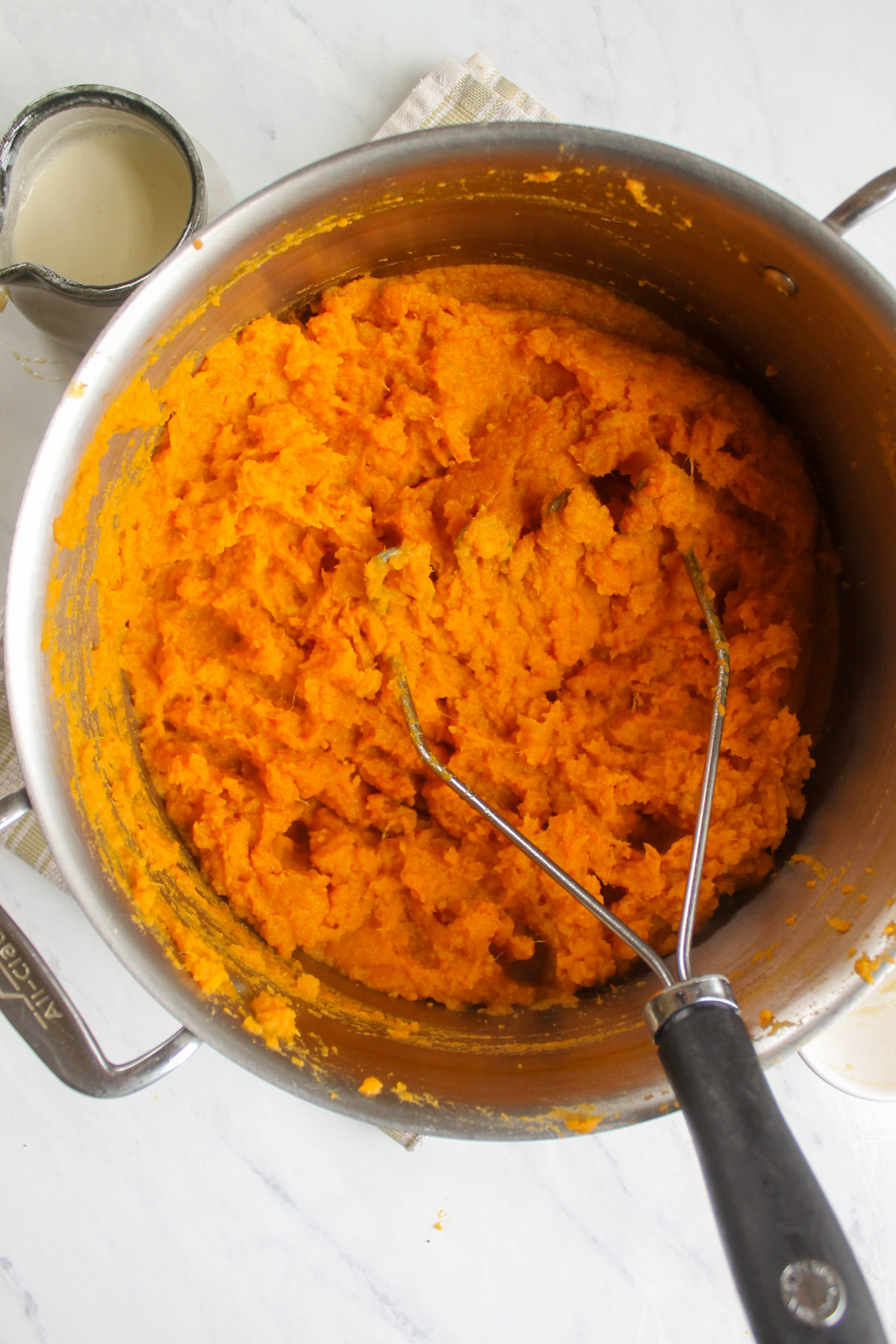 Mashing sweet potatoes in a pot with a potato masher.