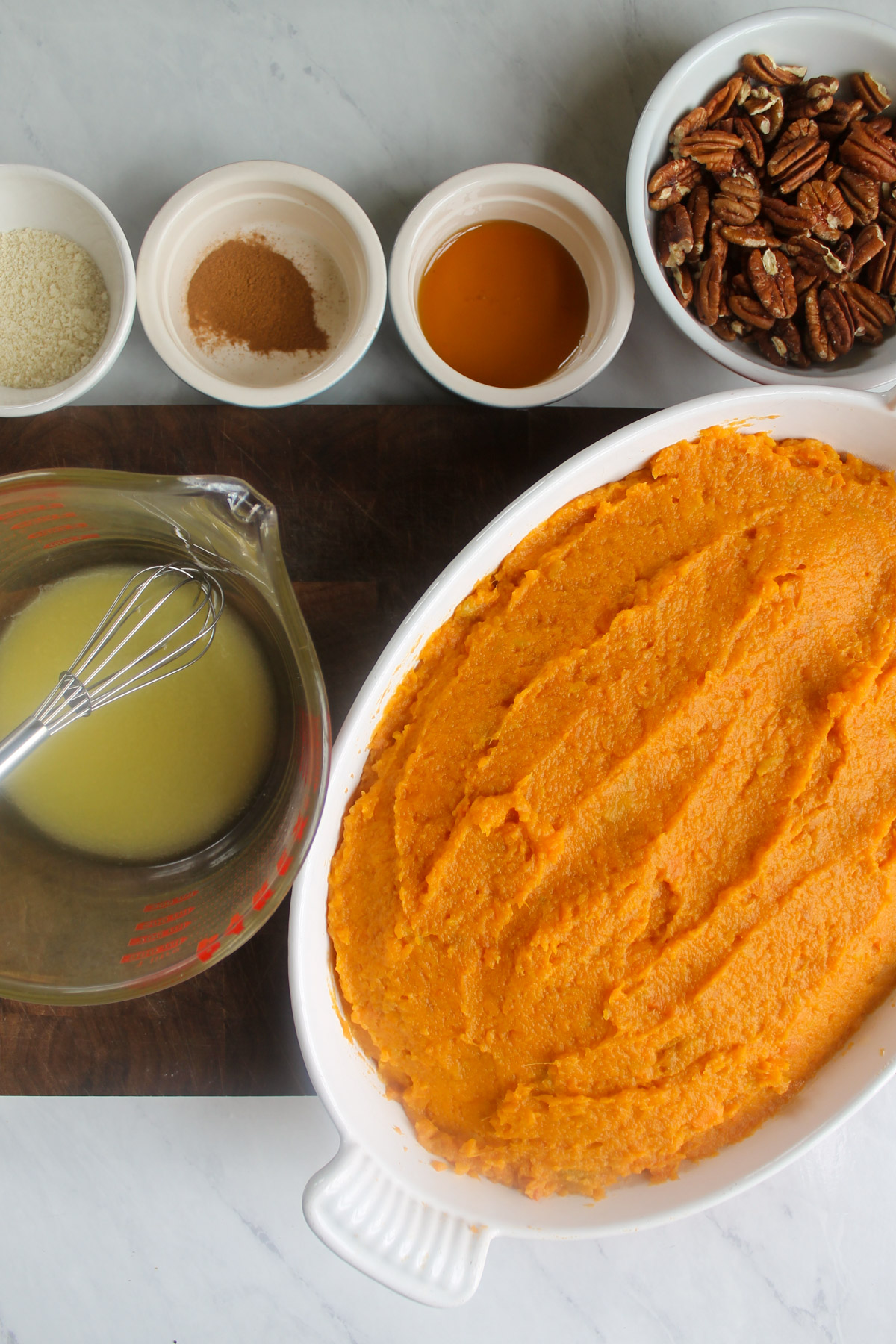 A baking dish with mashed sweet potatoes and ingredients to make maple pecan topping.
