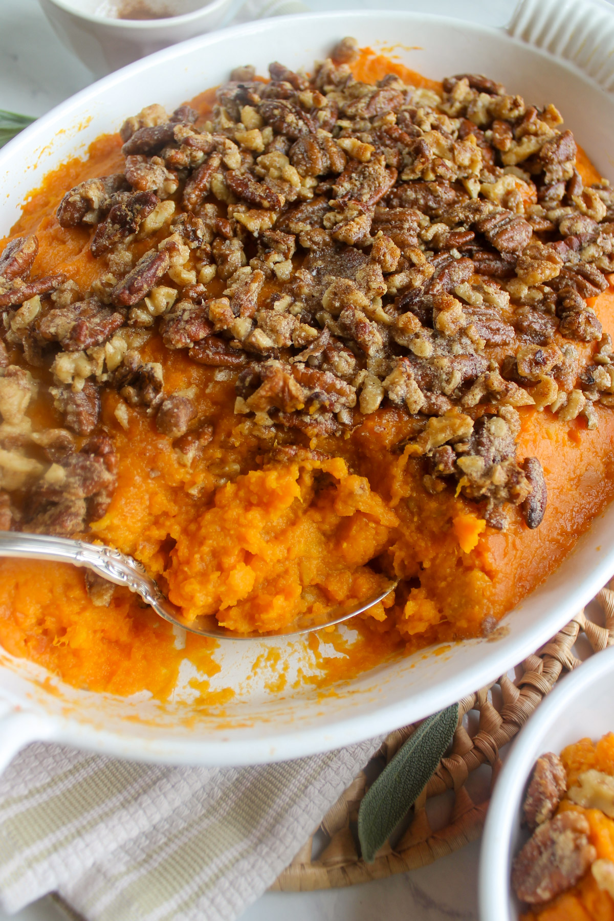 A spoon scooping sweet potato casserole with pecans out of a baking dish.