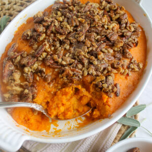 A baking dish of maple pecan sweet potato casserole served with a spoon.