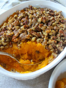 A spoon scooping out orange butternut squash with butter pecan topping.