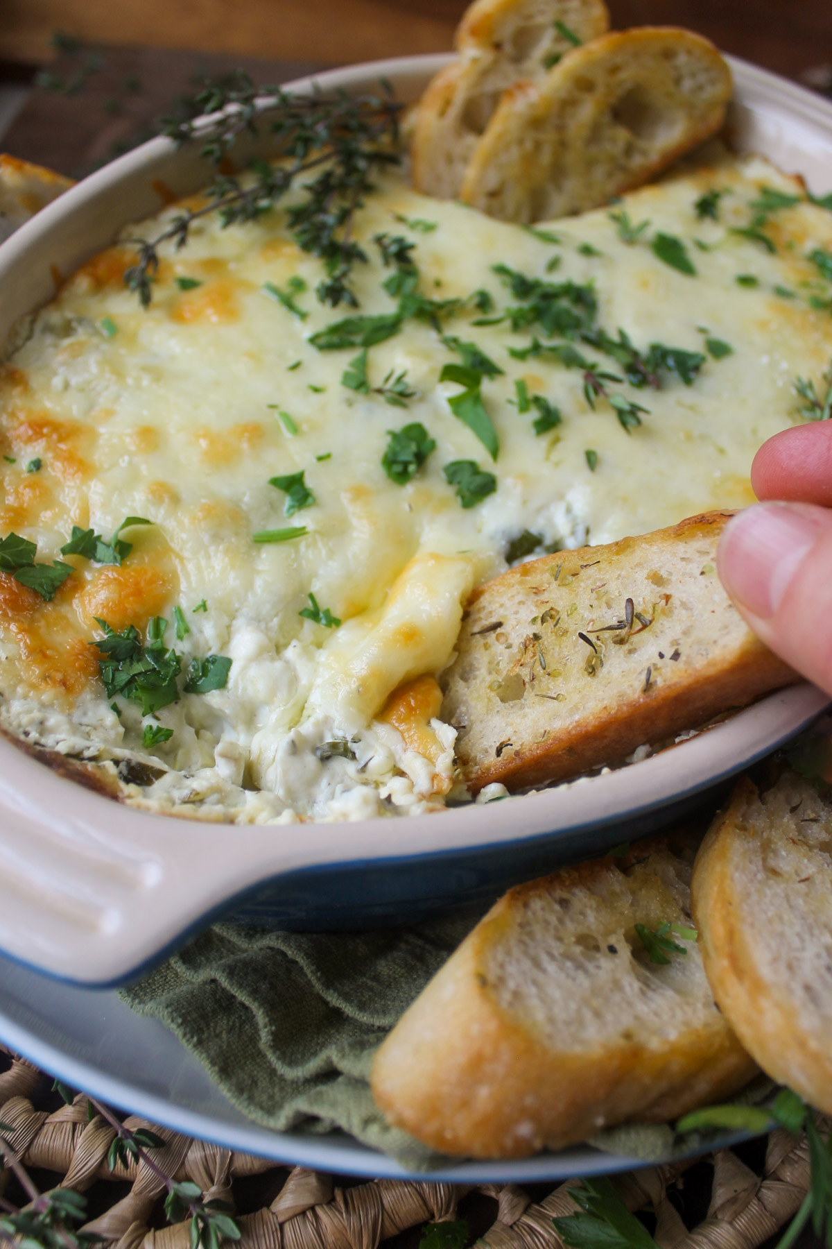 Fingers dipping crostini bread into cheesy artichoke dip.