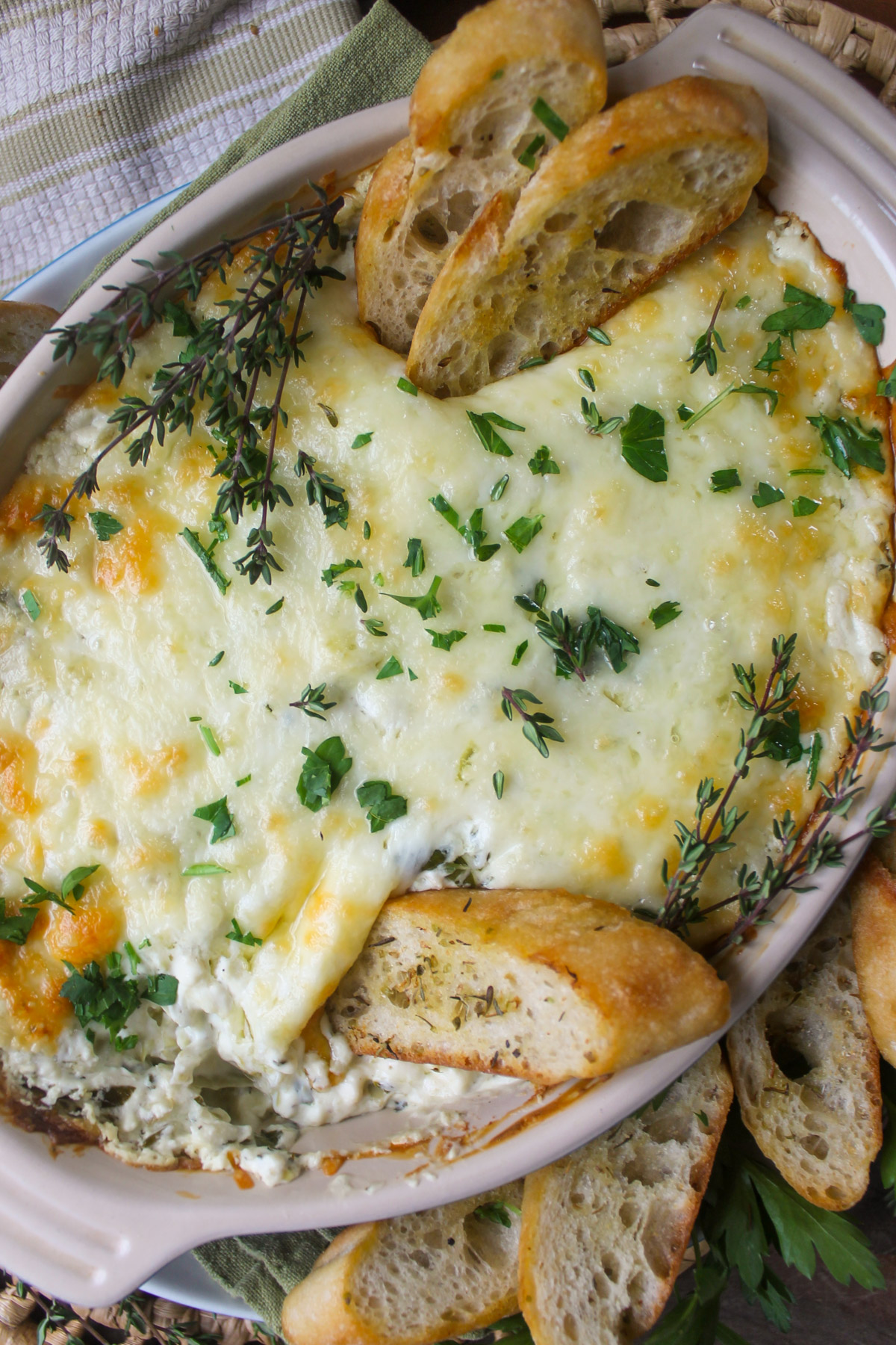 Baked goat cheese artichoke dip with green herbs and toasted baguette slices.