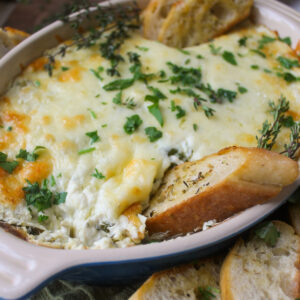 Baked goat cheese artichoke dip with spinach and herbs dipped with toasted bread.