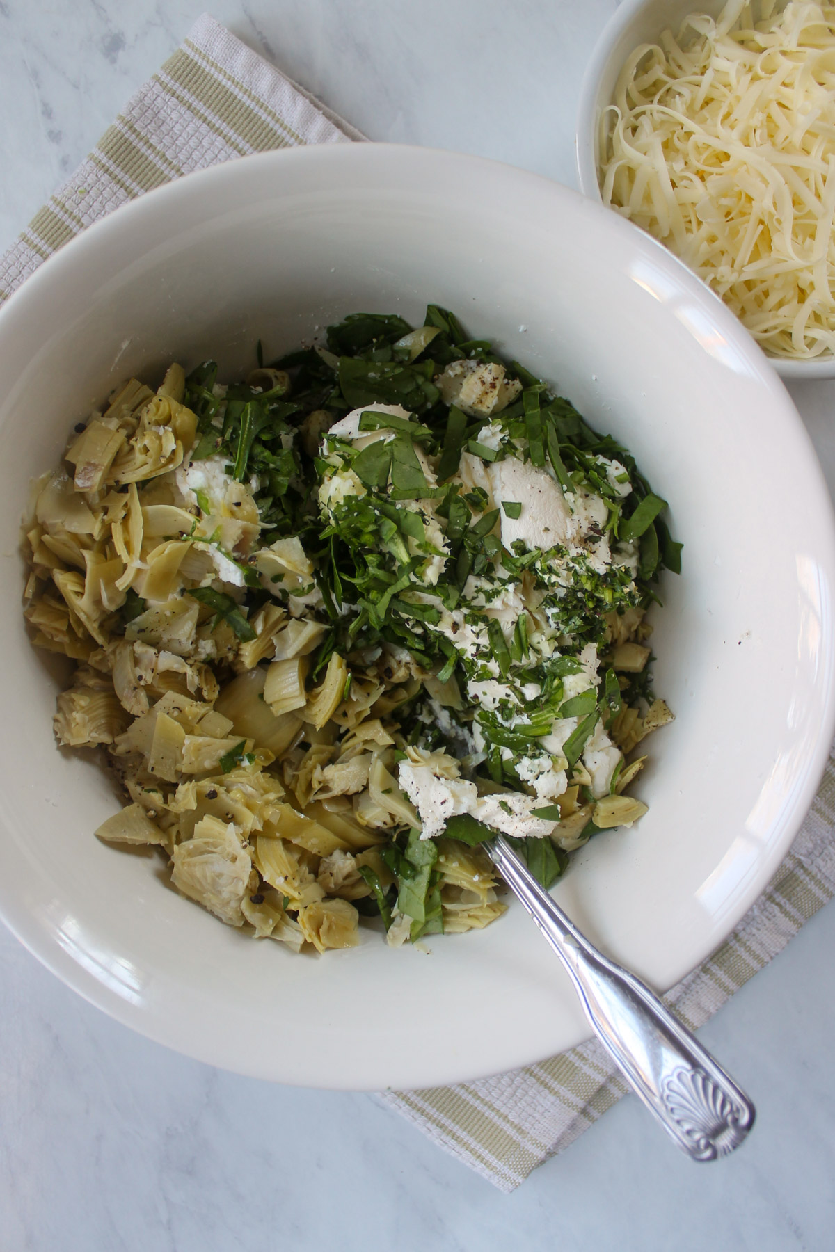 Goat cheese, cream cheese, artichokes, spinach and herbs in a white bowl.