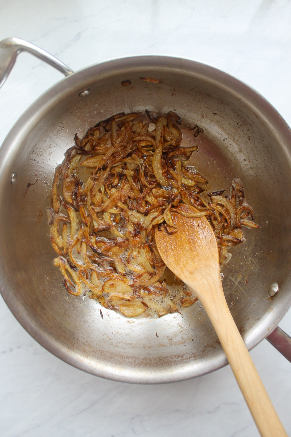 Caramelized onion slices in a skillet with a wooden spoon.