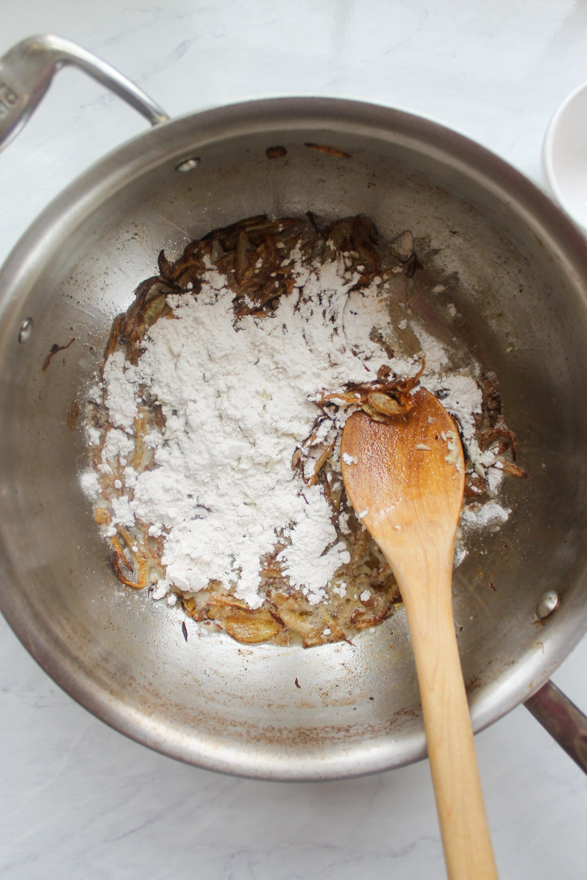 Adding flour and garlic to the buttery caramelized onions to form a roux.