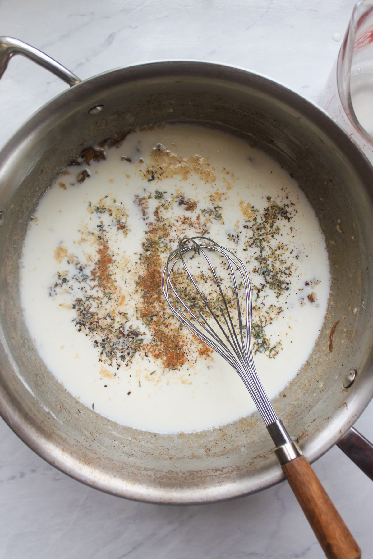 Milk and seasonings added to the roux in a skillet with a whisk.