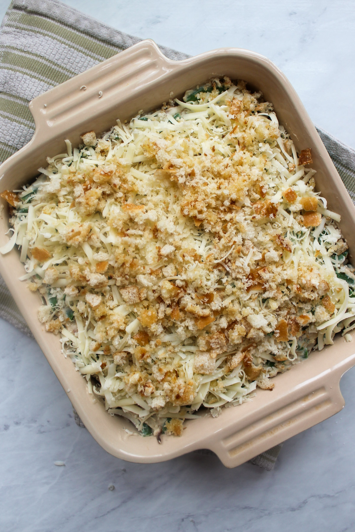Unbaked green bean au gratin casserole topped with cheese an breadcrumbs.