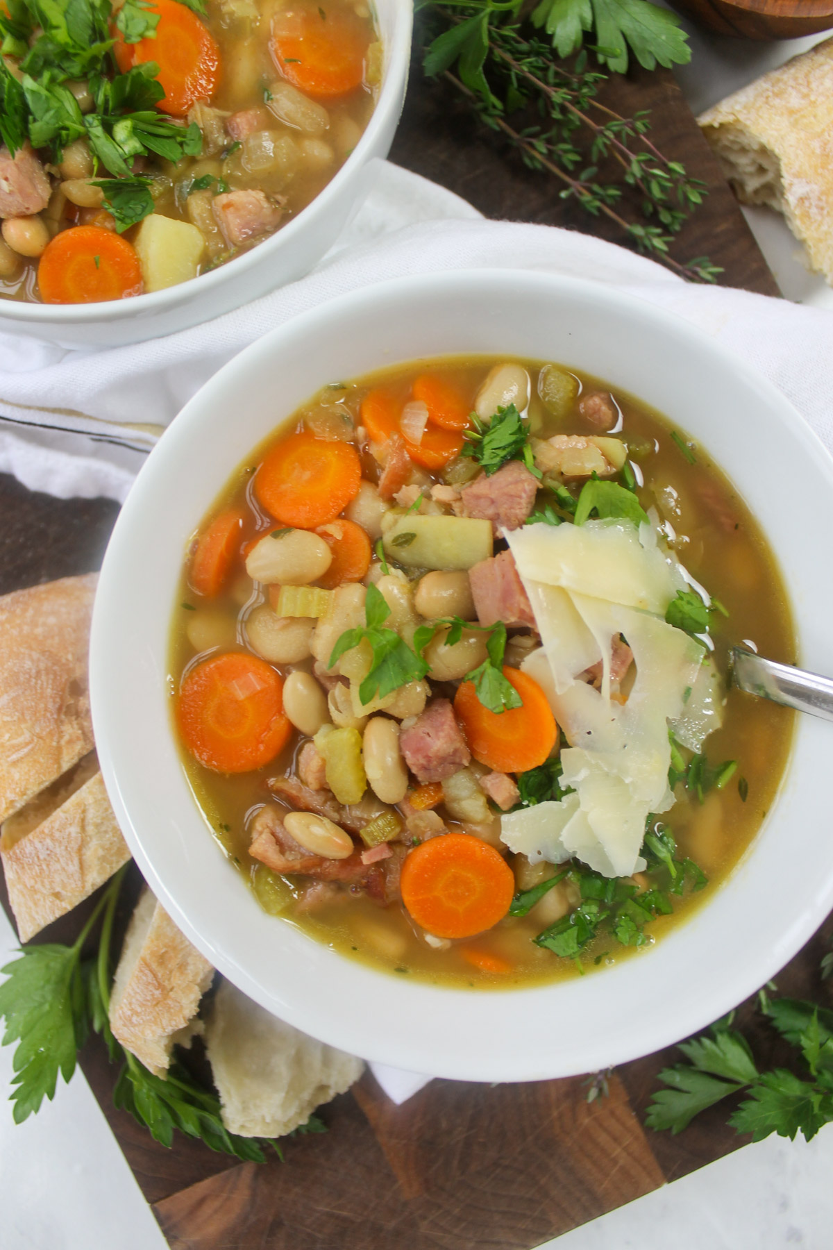 White bowls of hearty ham and white bean soup with carrots and topped with parsley.