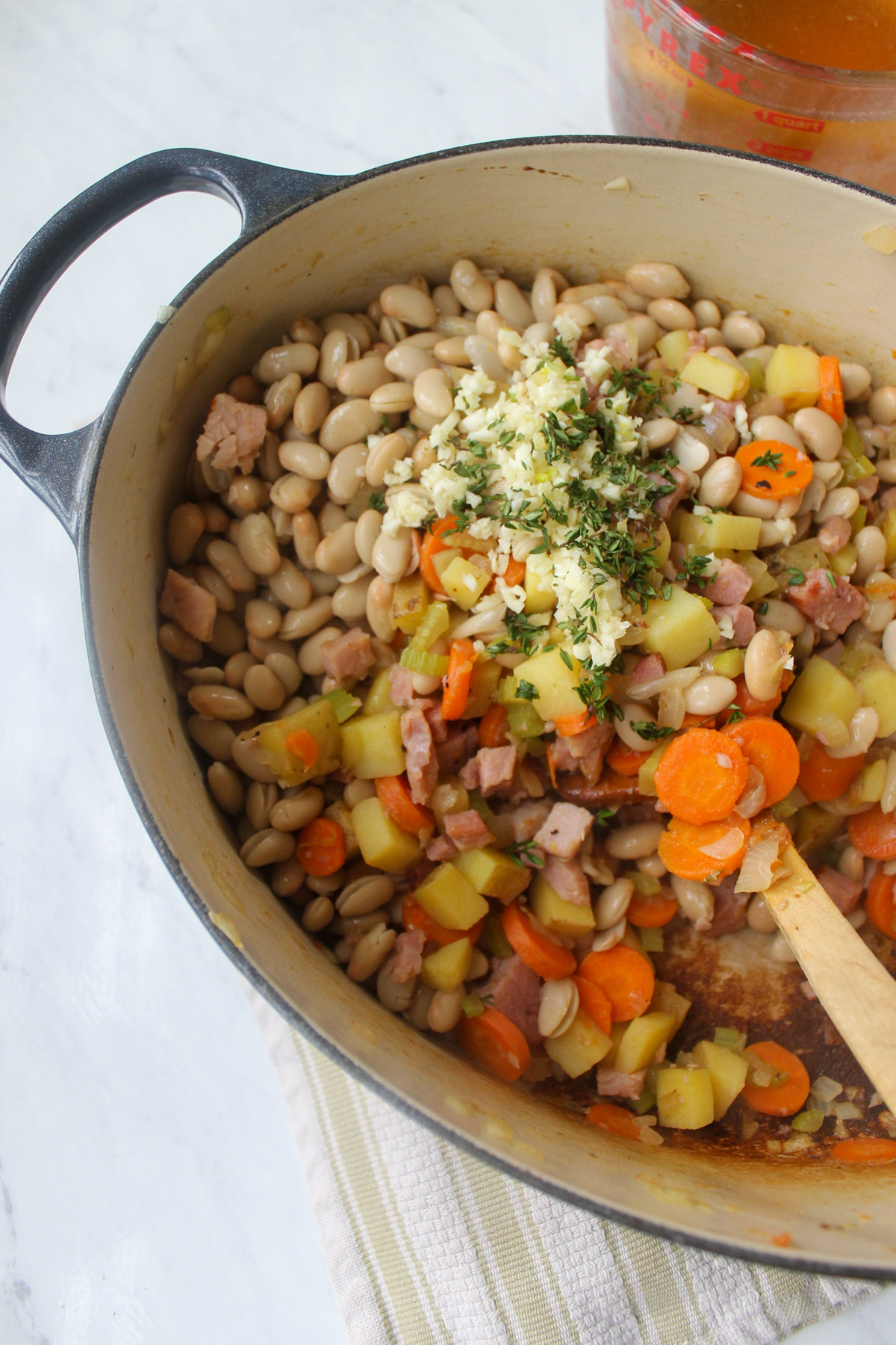 Adding white beans, garlic and fresh thyme to the soup pot with the veggies and ham.