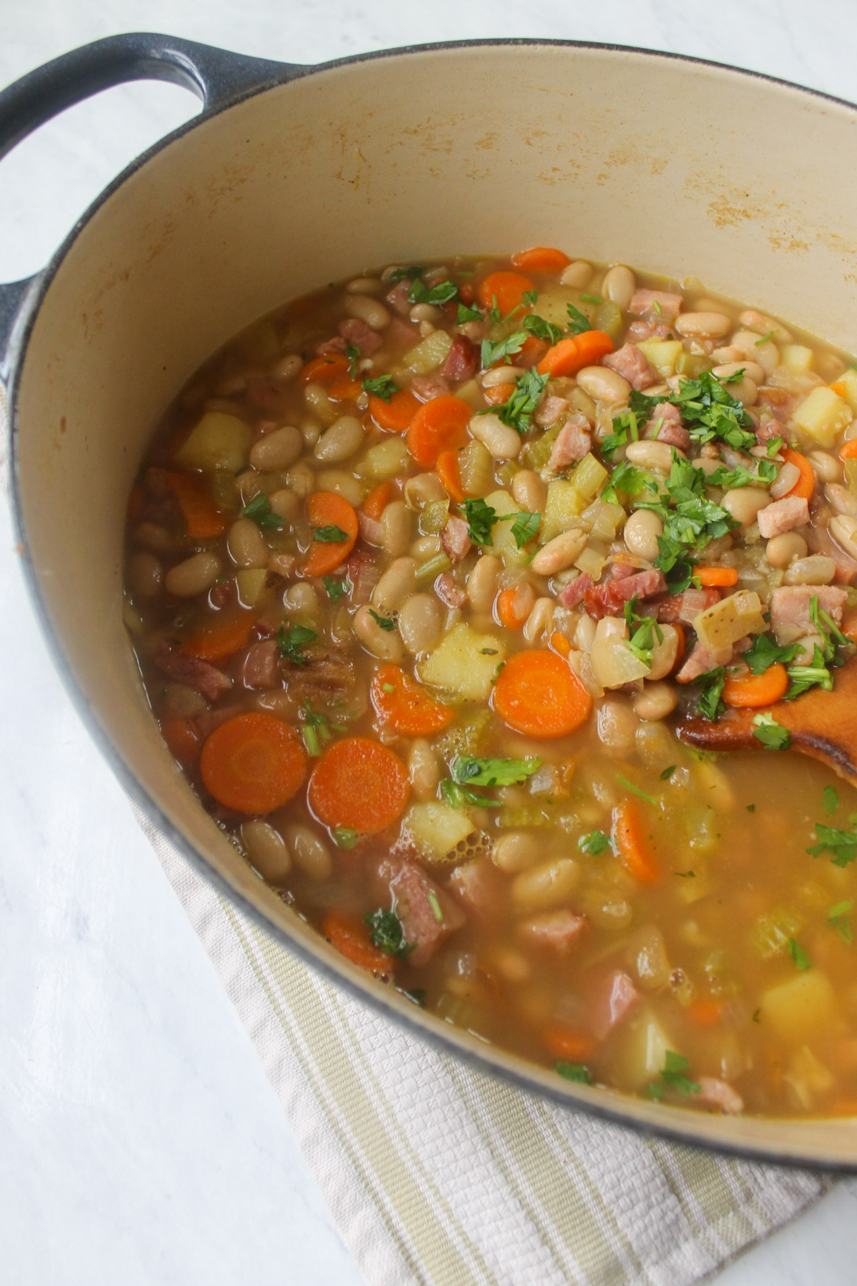 A soup pot of Ham and White Bean Soup with a wooden spoon.