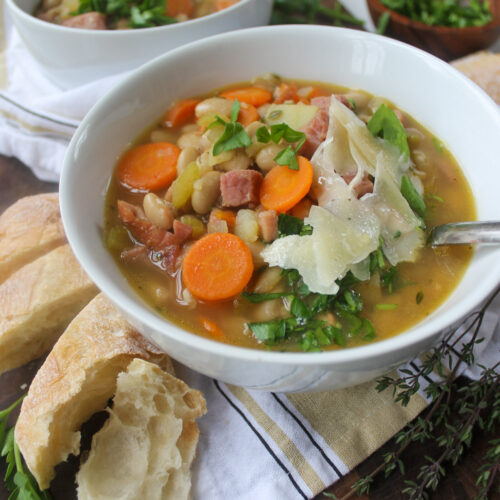 A bowl of White Bean Soup with Ham with veggies and crusty bread on the side.