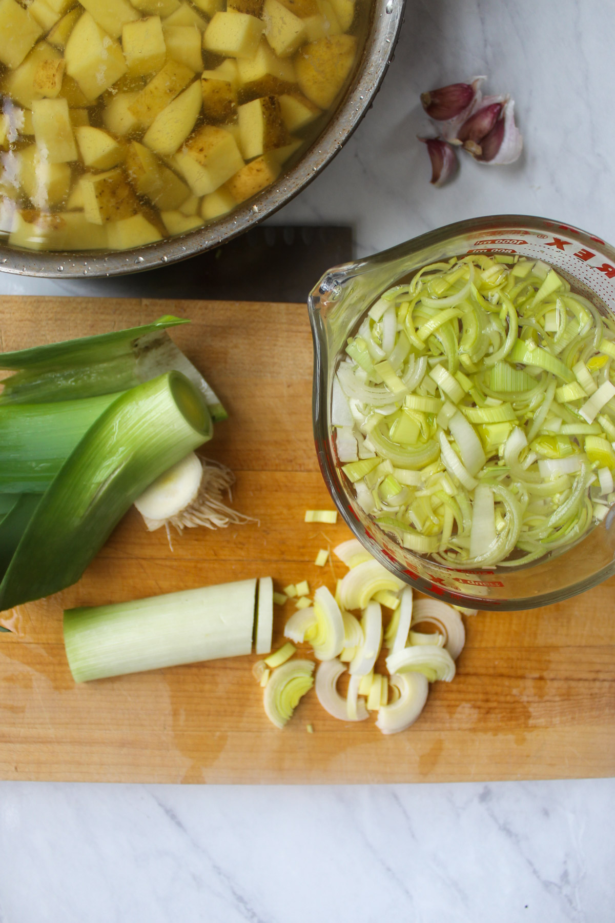 Slicing leeks on a cutting board into a bowl of water to wash off dirt.