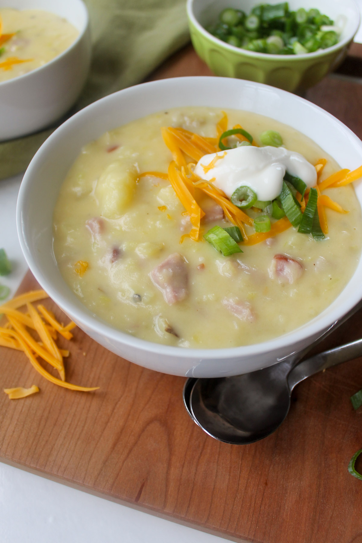 A bowl of creamy Potato Ham & Leek Soup with toppings.