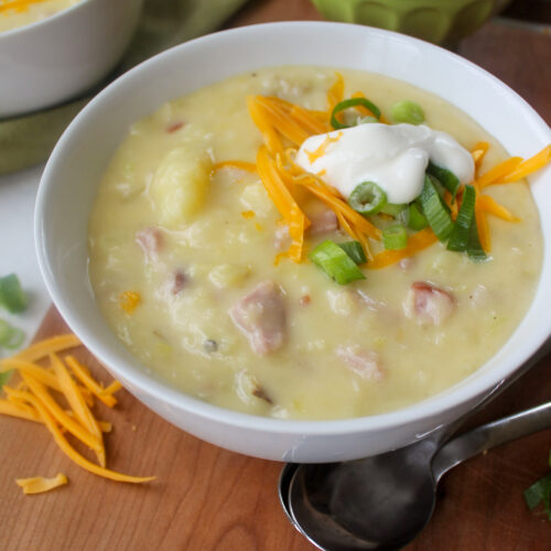 Potato Ham Leek Soup in a white bowl with cheese and green onion slices.