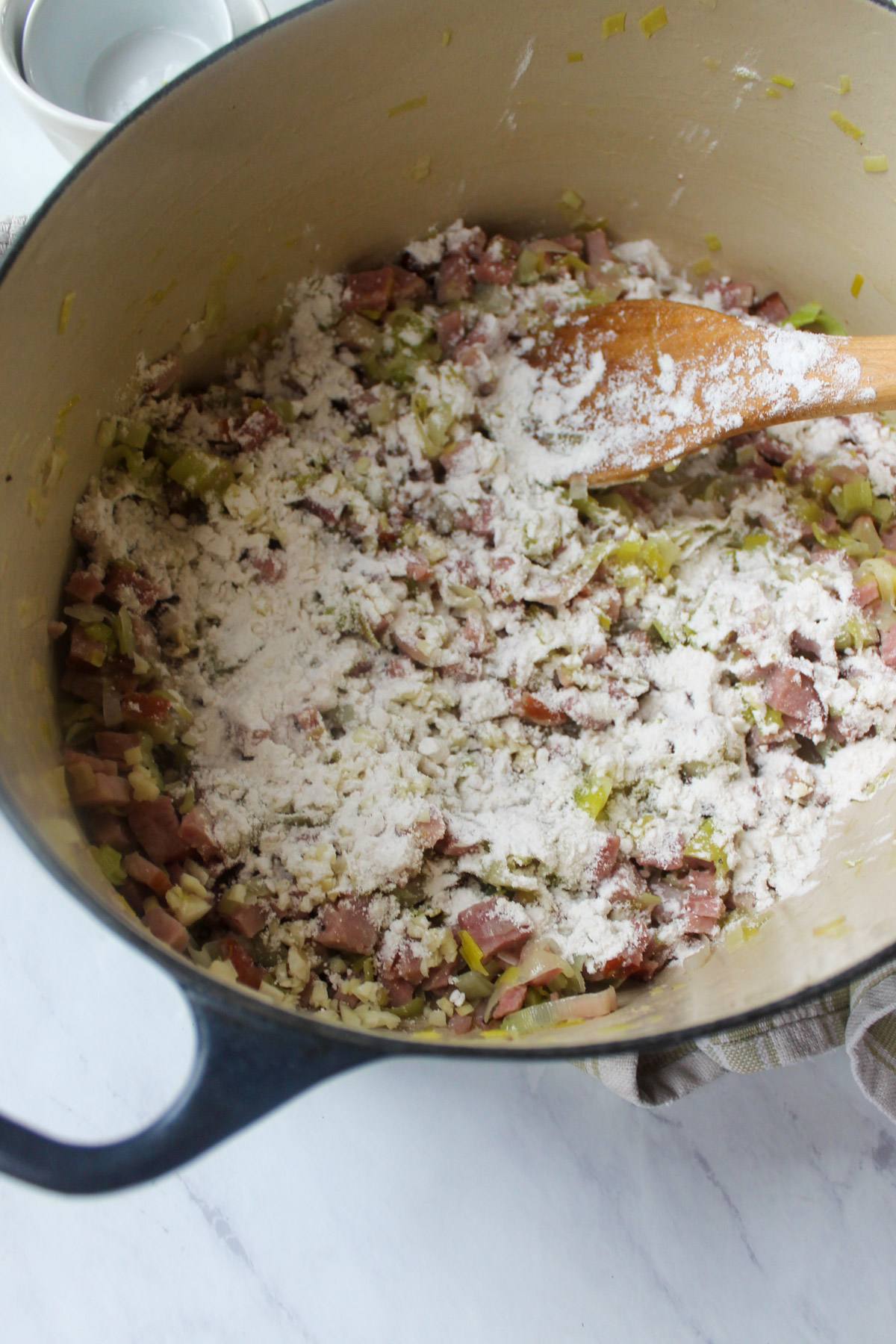 Adding flour to the cooked leeks and ham to make a roux to thicken the soup.