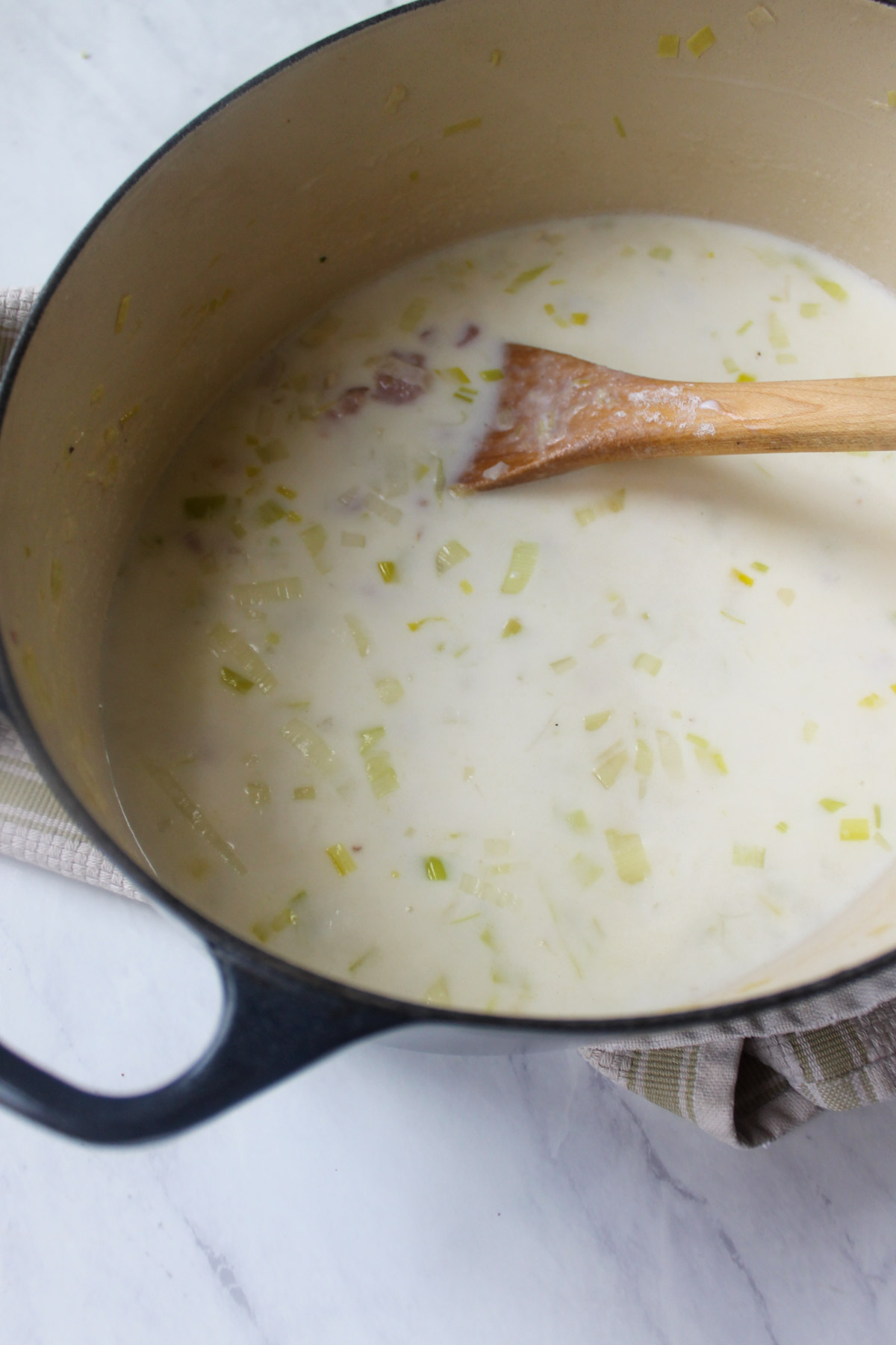 Adding milk and starchy water from the potatoes to the soup.