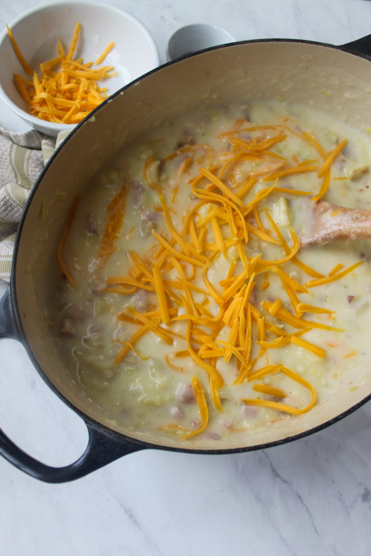 Adding shredded cheddar cheese to the potato ham soup.