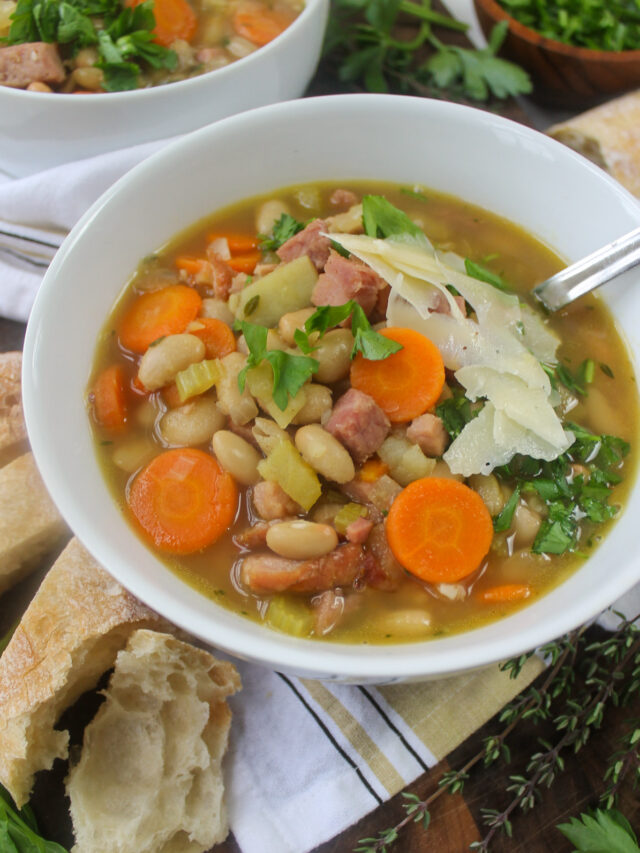 A bowl of white bean soup with ham topped with Parmesan cheese and fresh parsley.