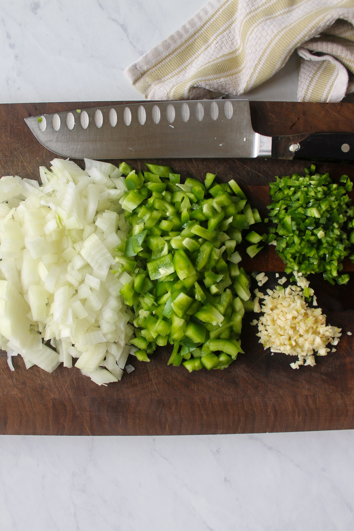 Chopped onion, green bell pepper, jalapeno pepper, and garlic on a wooden cutting board.