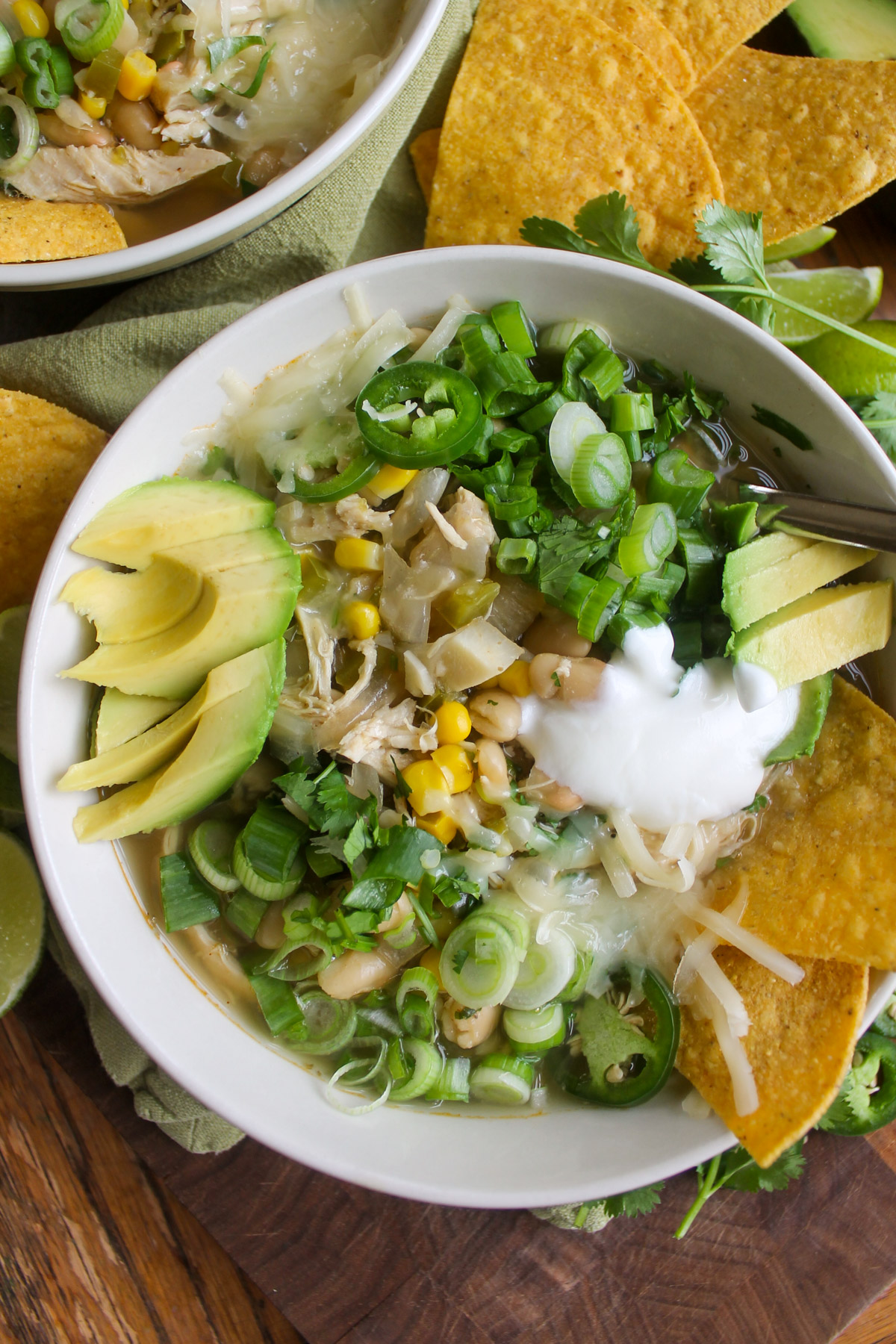 A bowl of white chicken chili with sliced jalapeno, cheese, yogurt, avocado and tortilla chips.