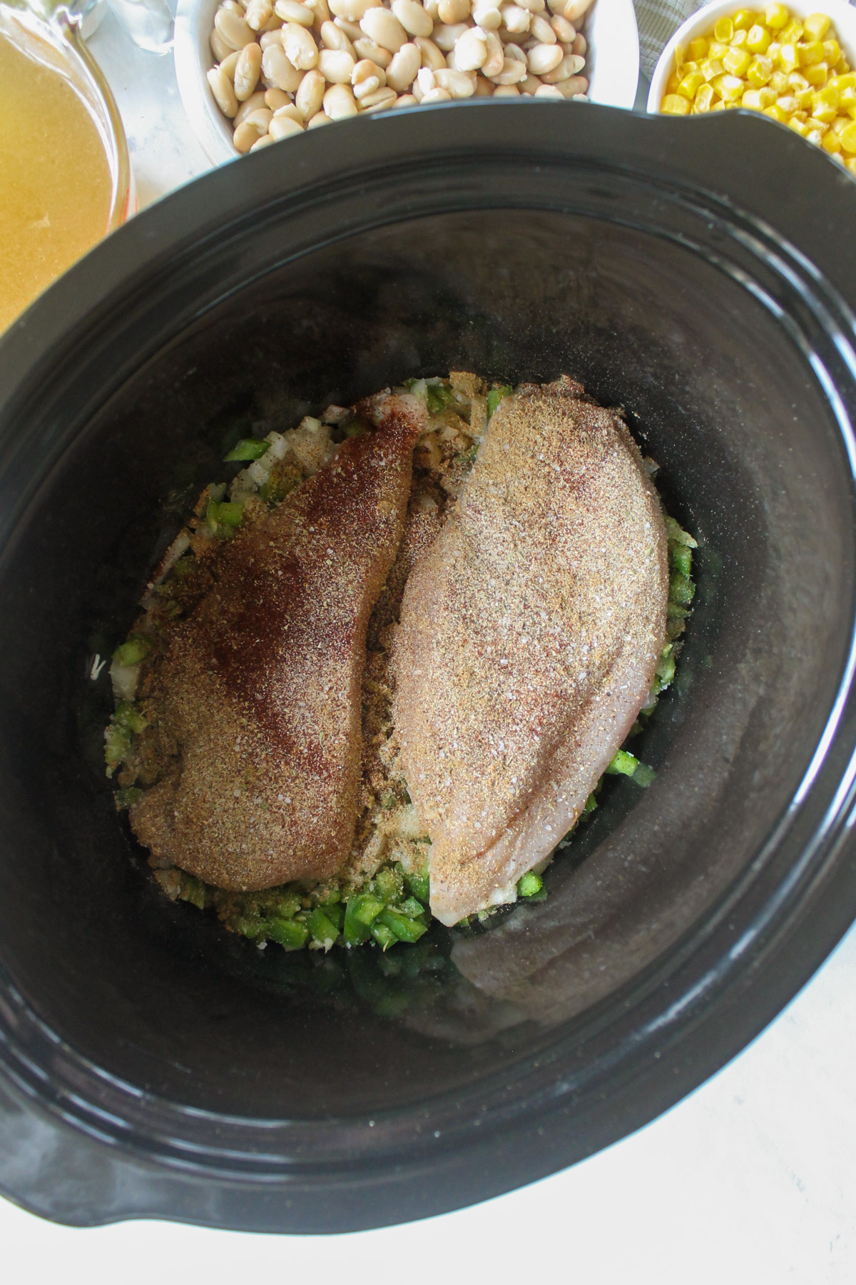 Chicken breasts with seasoning in a crockpot with onions and green peppers.