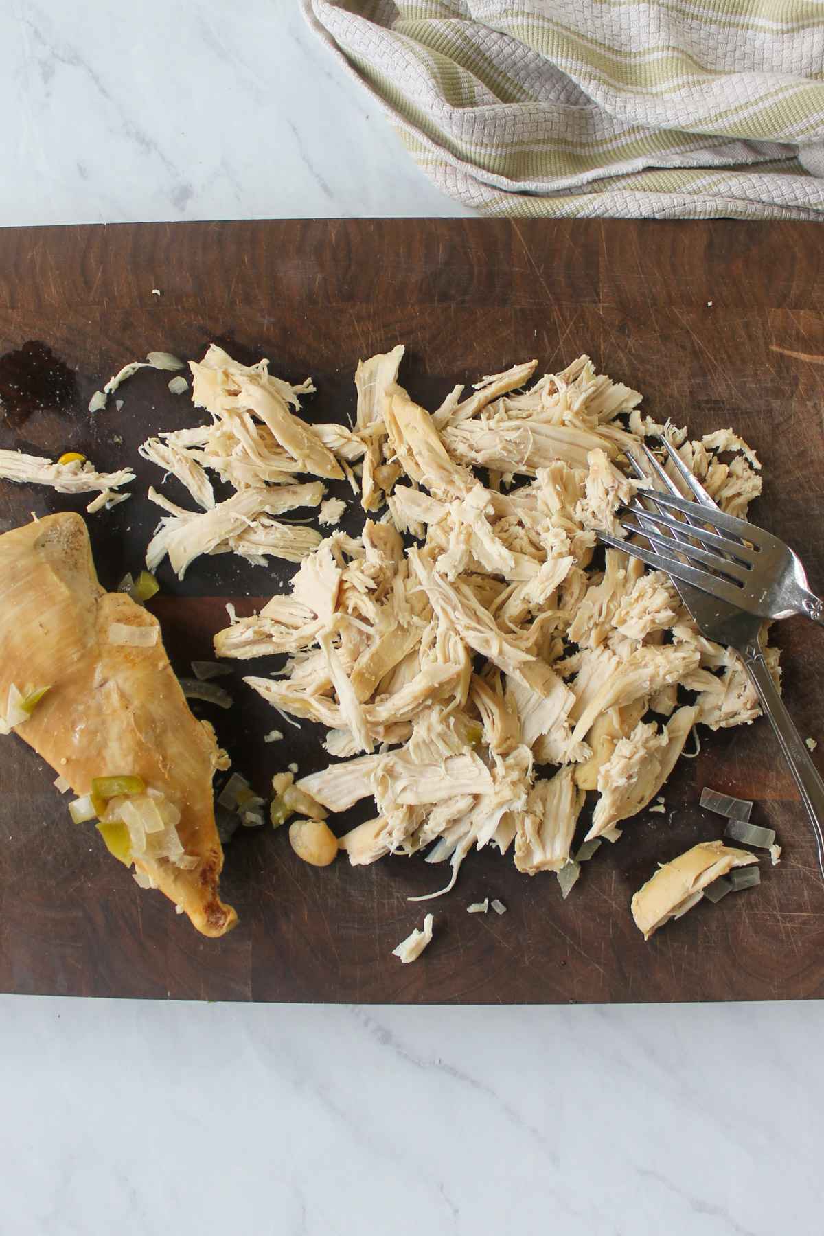 Shredding cooked chicken breasts on a cutting board with 2 forks.