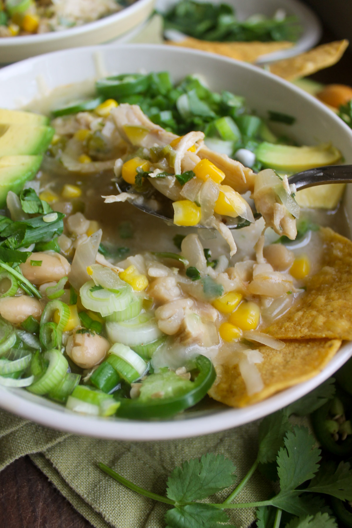 A white bowl of white chicken chili with a spoon lifting the shredded chicken and corn.