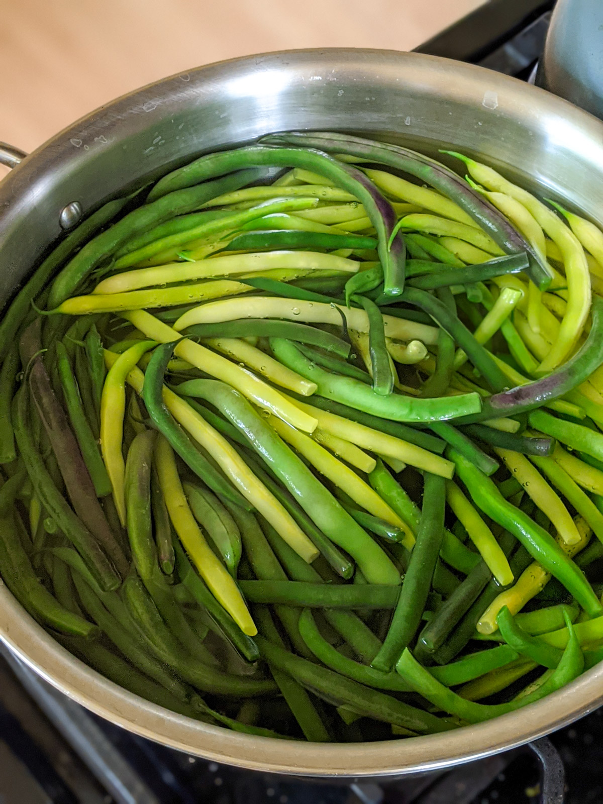 Yellow and green beans being blanched in a pot of water.