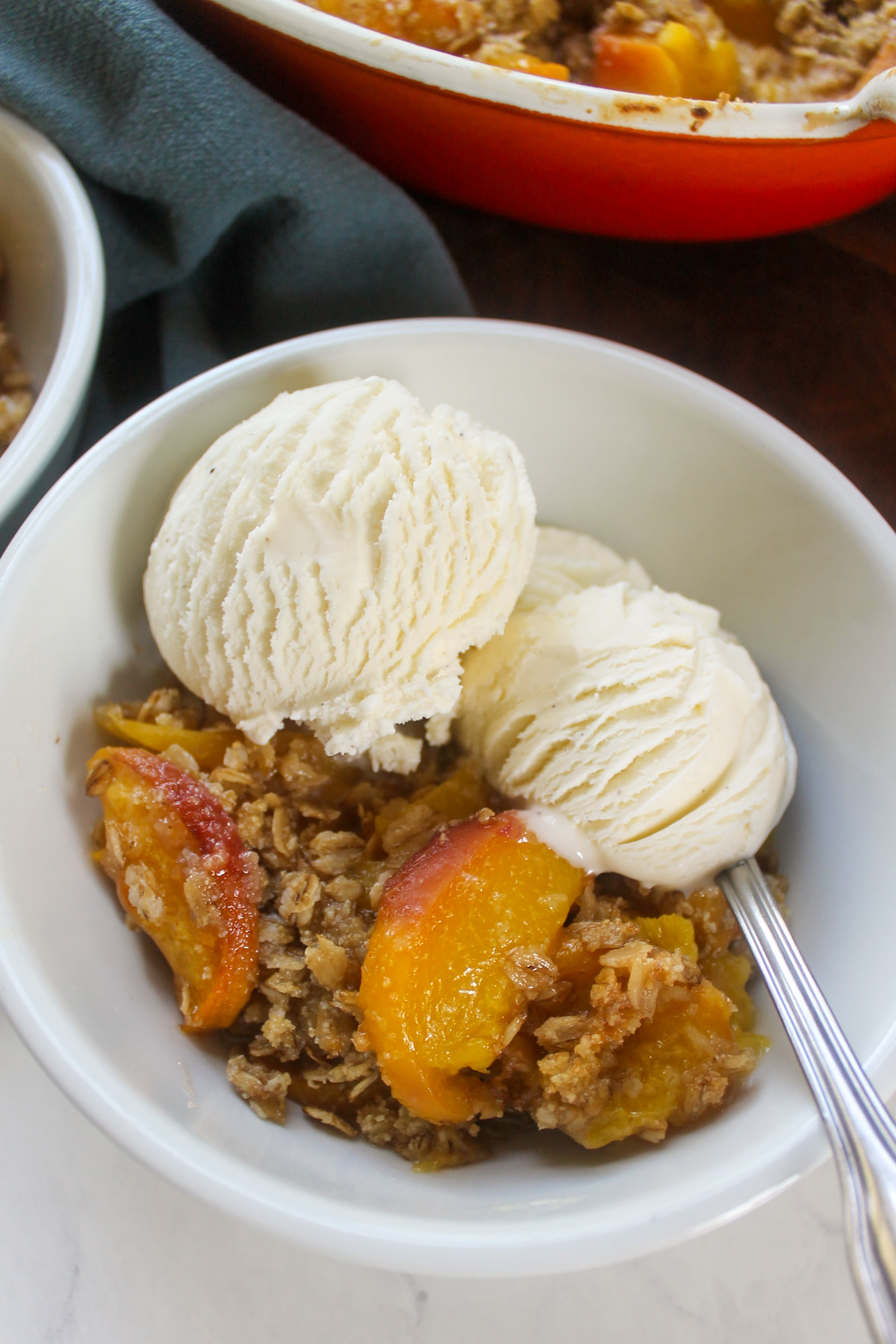 A bowl of baked peach crisp dessert with two scoops of vanilla ice cream.