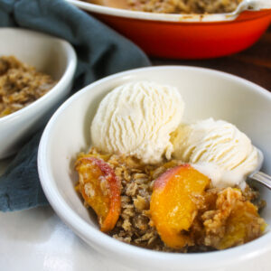 Peach crisp in a bowl with vanilla ice cream and a spoon.