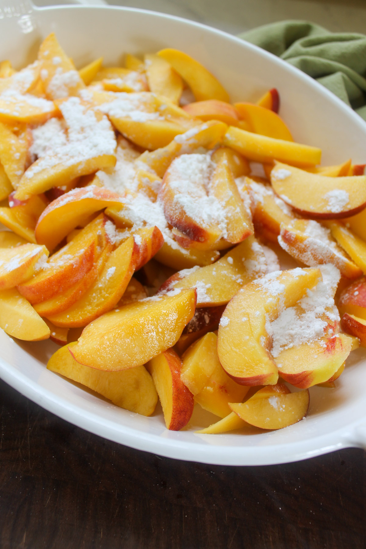 Fresh sliced peaches in an oval baking dish sprinkled with sugar and cornstarch.