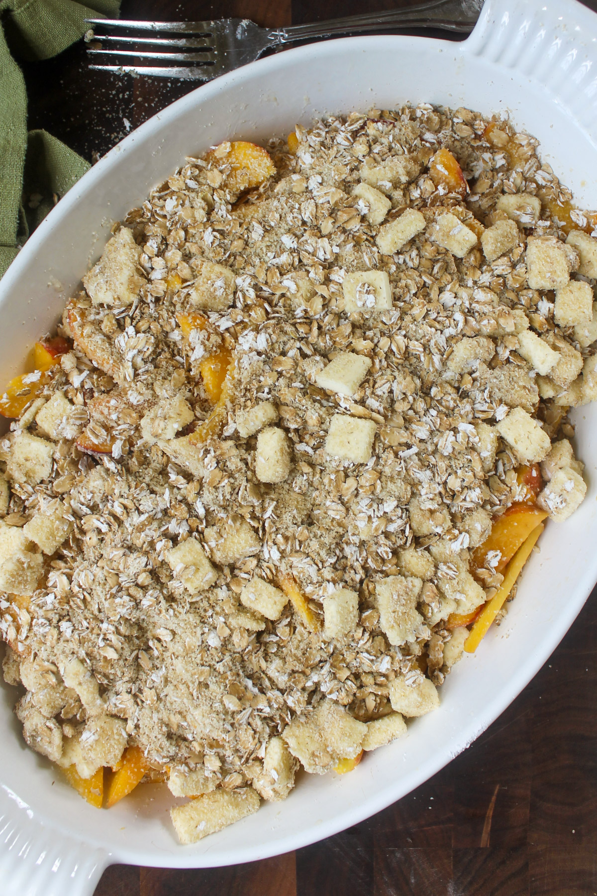 Unbaked peach crisp with the oat mixture poured over the peaches in a baking dish.