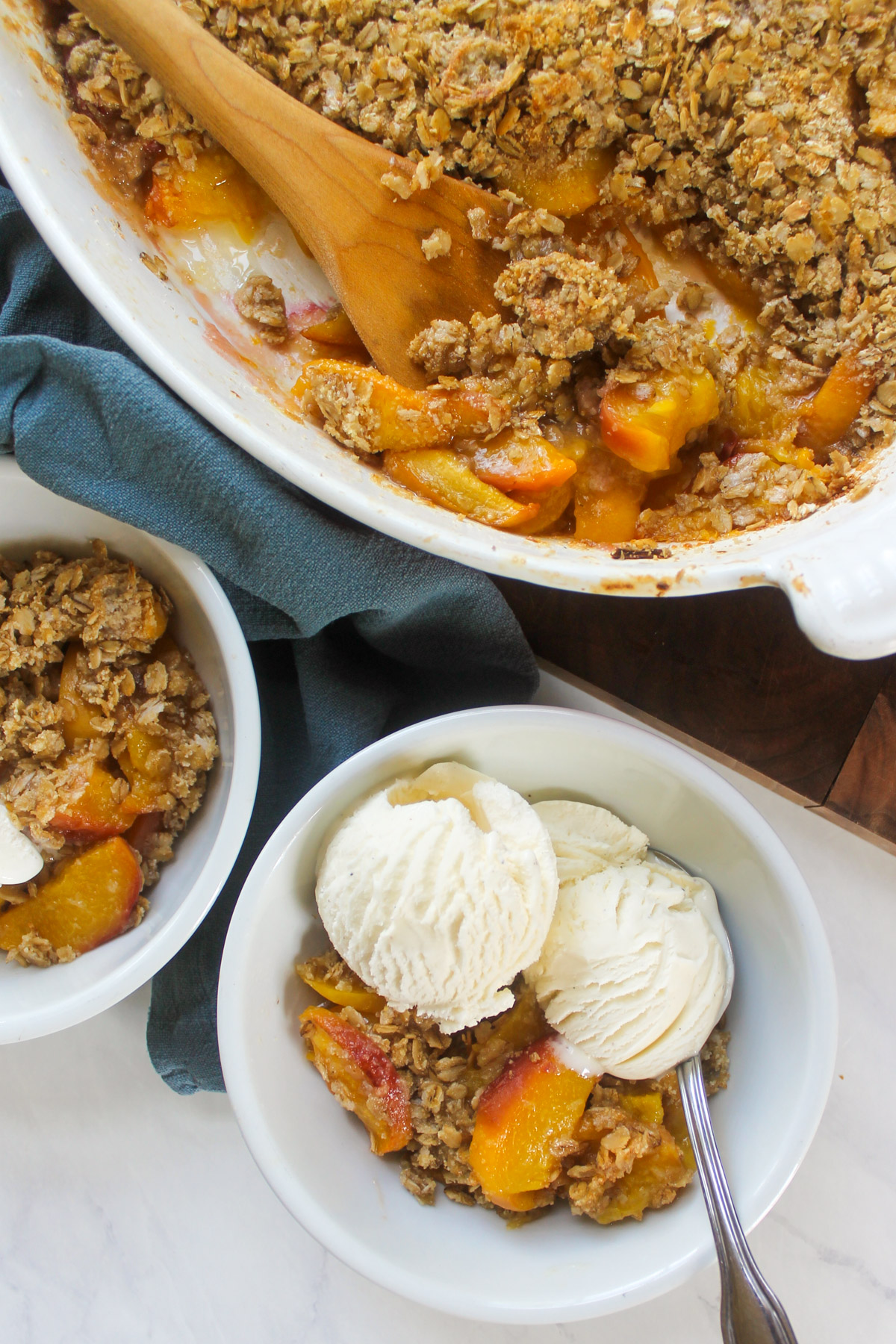A bowl of peach crisp with vanilla ice cream next to the baking dish.